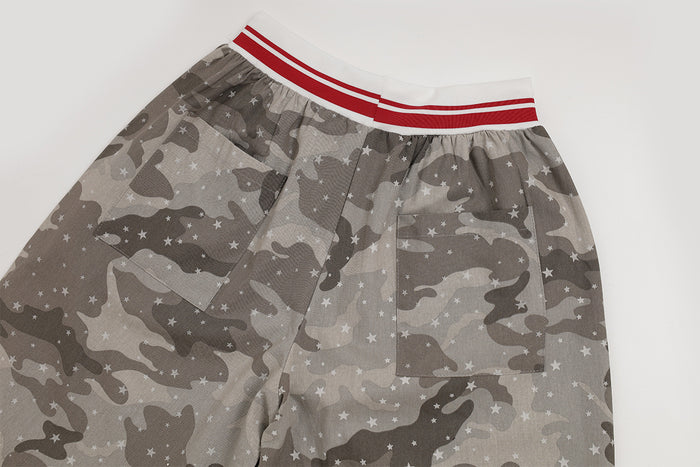 Upper front section of gray star-print camouflage cargo pants showing the red-striped waistband and side pocket