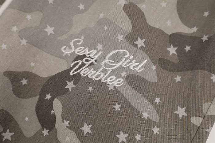 Close-up of white cursive lettering embroidered on gray camouflage fabric among scattered star motifs