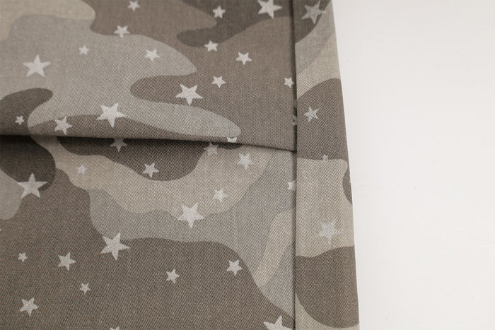 Close-up of a stitched flap pocket and side seam on gray camouflage pants with white star details