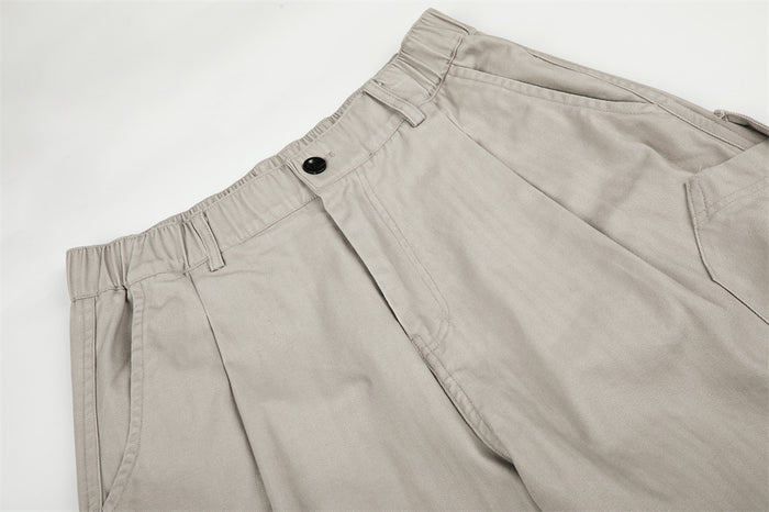 Beige pants waistband with button, belt loops, and front pleats close-up