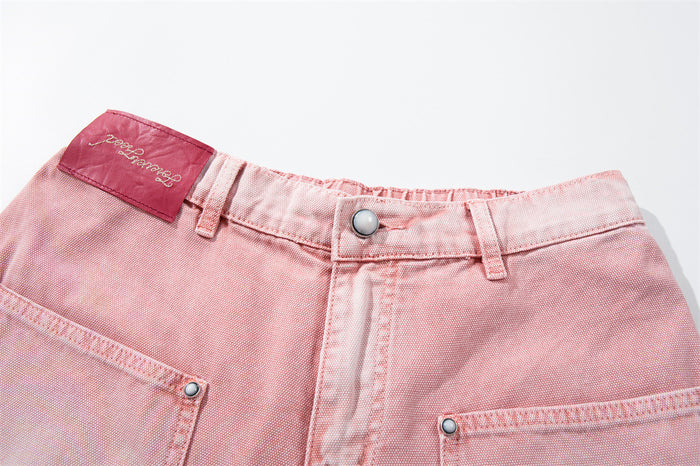 Close-up of waistband on pink washed carpenter jeans with belt loops, button closure, and red label
