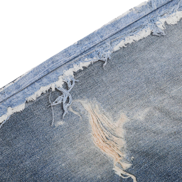 Close-up of denim fabric showing faded wash and torn frayed rip detail