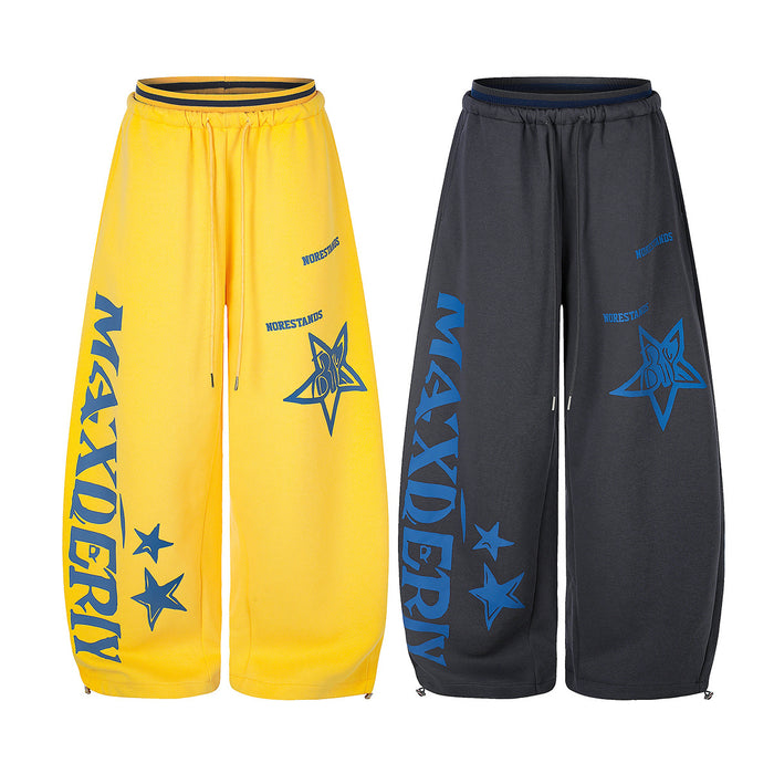 Front view of yellow and charcoal wide-leg sweatpants with blue star graphics, text, and drawstring waists