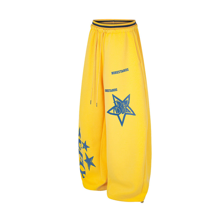 Angled front view of yellow wide-leg sweatpants with blue star emblem, text, and adjustable drawstring waist