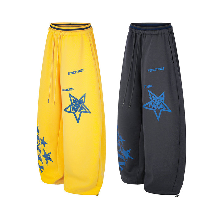Angled front views of yellow and charcoal wide-leg sweatpants with matching blue star graphics and drawstrings