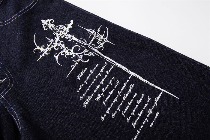 Close-up of white Gothic cross and script embroidery on dark indigo denim leg