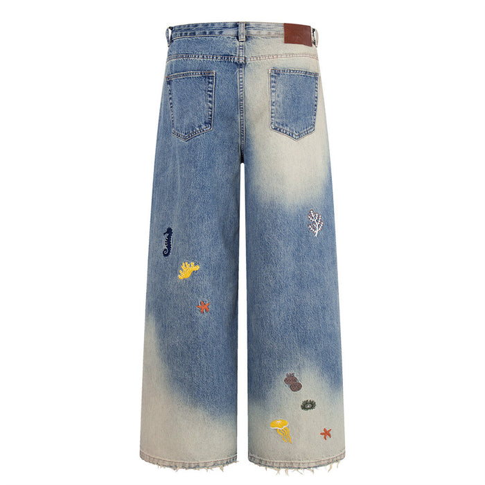 Back flat lay of wide-leg jeans with gradient wash, ocean embroidery, and brown patch waistband detail
