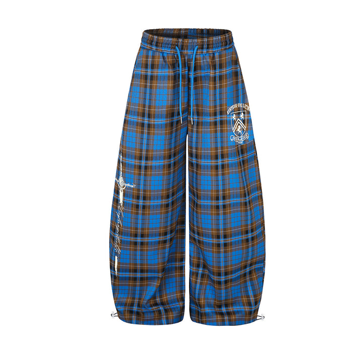 Front view of wide-leg blue and brown plaid pants with blue drawstring, white crest graphics, and gathered hems