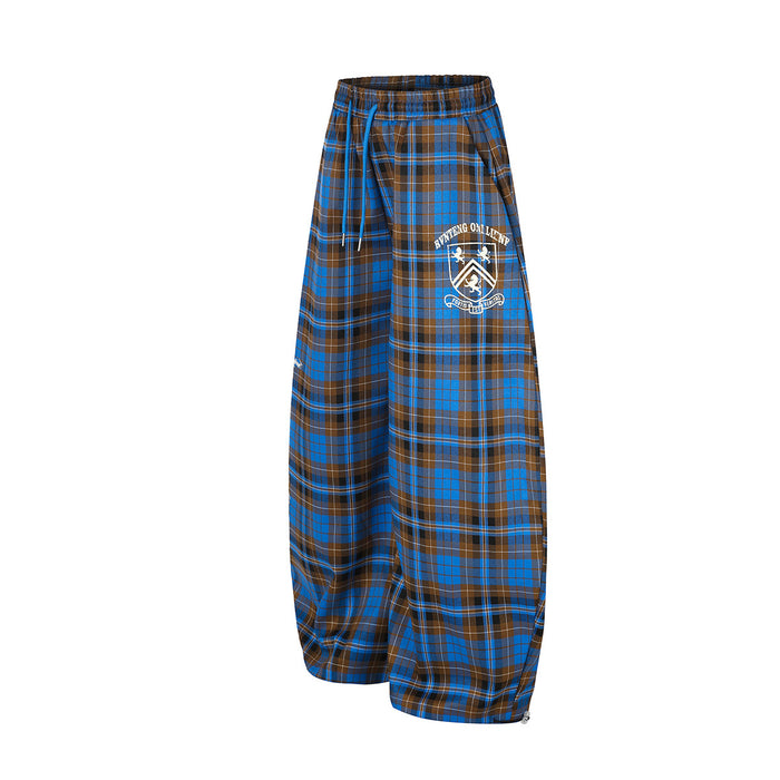 Angled front view of blue and brown tartan wide-leg pants showing the white crest graphic and drawstring waist