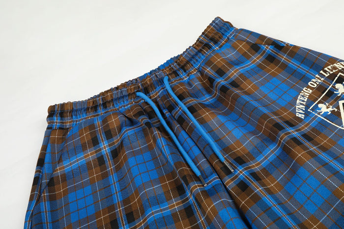 Close-up of the plaid pants waistband with blue drawstring and partial white crest graphic