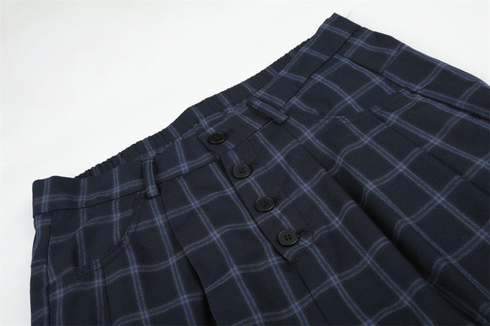 Close-up of the front waistband and button-fly detail on navy plaid trousers