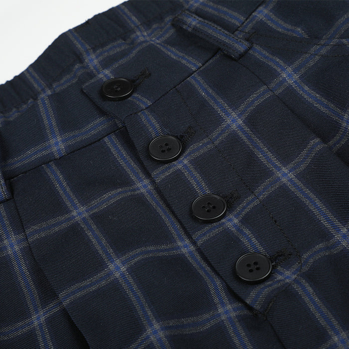 Close-up of four black buttons on the button-fly front of navy plaid trousers