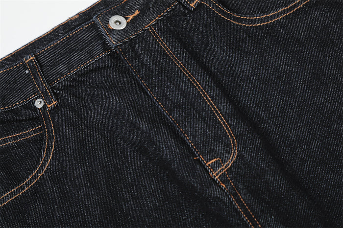 Close-up of front fly and diagonal seam detail on dark raw denim jeans