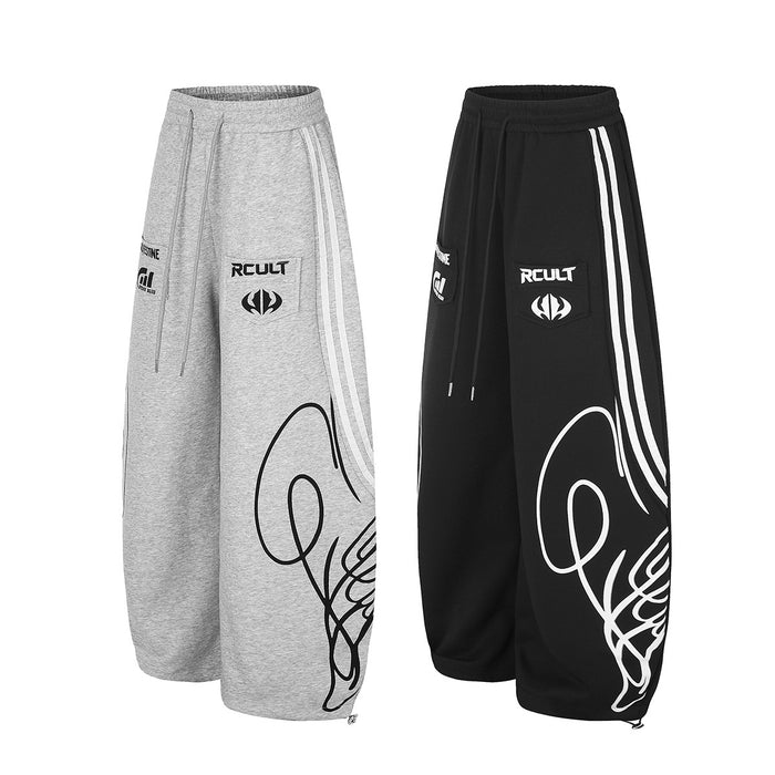 Angled front view of matching heather gray and black wide-leg sweatpants with white stripes and graphic prints