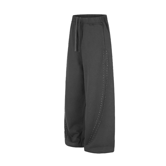 Angled side view of black wide-leg sweatpants highlighting the curved rows of side studs