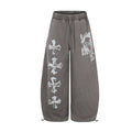 Wide-leg acid-washed sweatpants with distressed cross graphic print on left leg and face print on right thigh, shown in washe