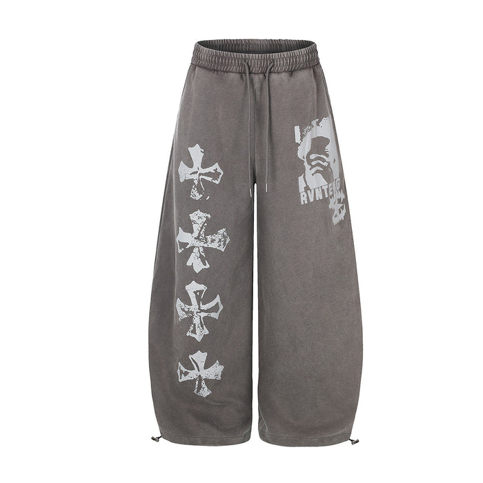 Wide-leg acid-washed sweatpants with distressed cross graphic print on left leg and face print on right thigh, shown in washe