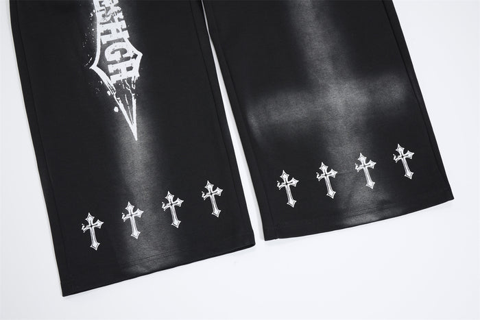 Close-up of black sweatpants hems showing repeated white cross prints and part of the front graphic