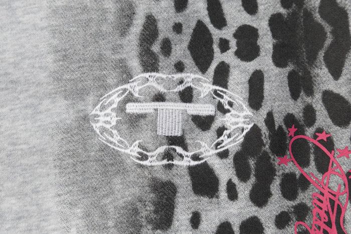 Close-up of a white embroidered oval badge with star details beside a pink graphic on leopard print