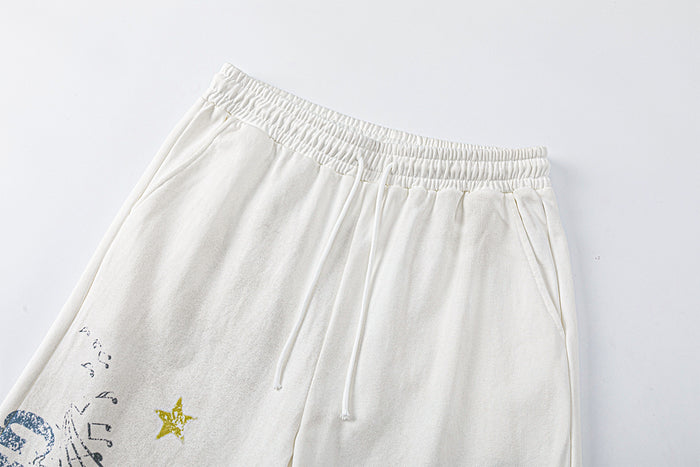 Close-up of cream sweatpants showing the elastic waistband, drawstring, side pocket, and partial graphic