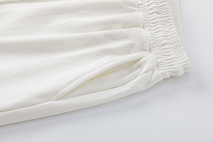 Close-up of cream sweatpants fabric with an elastic edge, stitched seam, and pocket opening