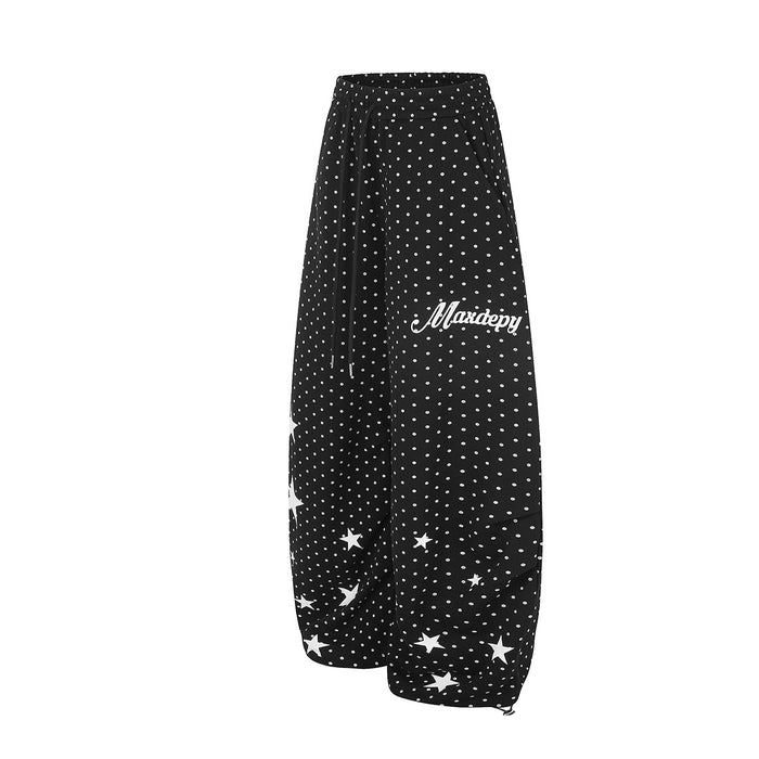 Side view of black wide-leg sweatpants with white polka dots, star accents, and white script text
