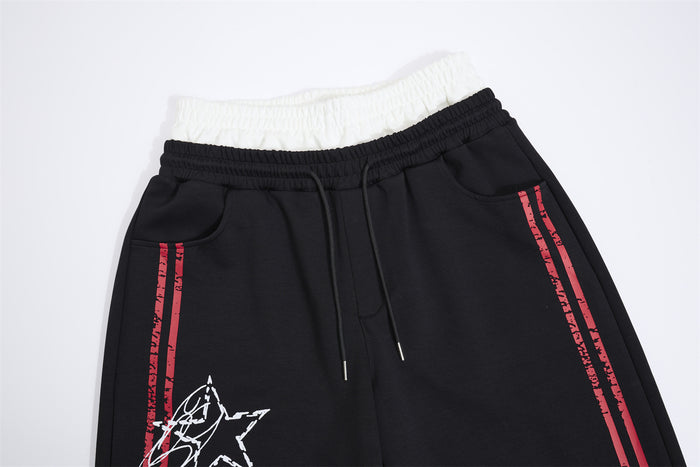 Close-up of black sweatpants upper front with white layered waistband, drawstring and red side stripes