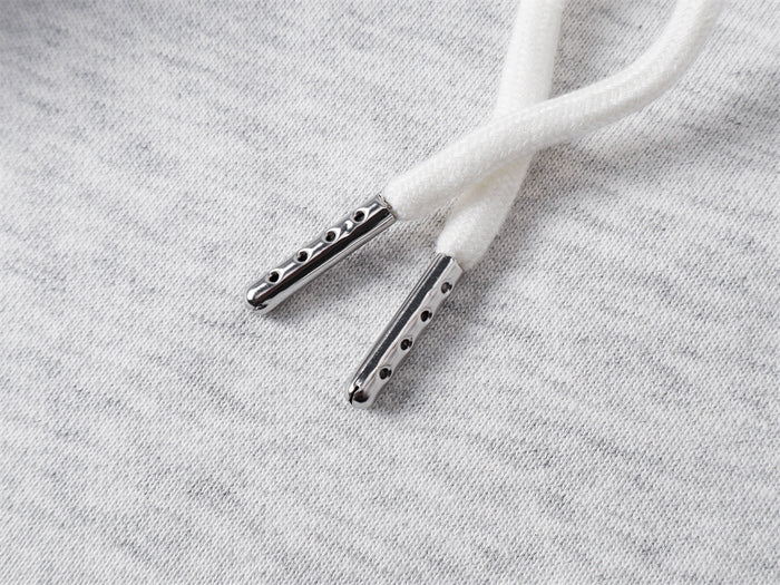 Close-up of white drawstring ends with silver metal aglets resting on light gray fabric
