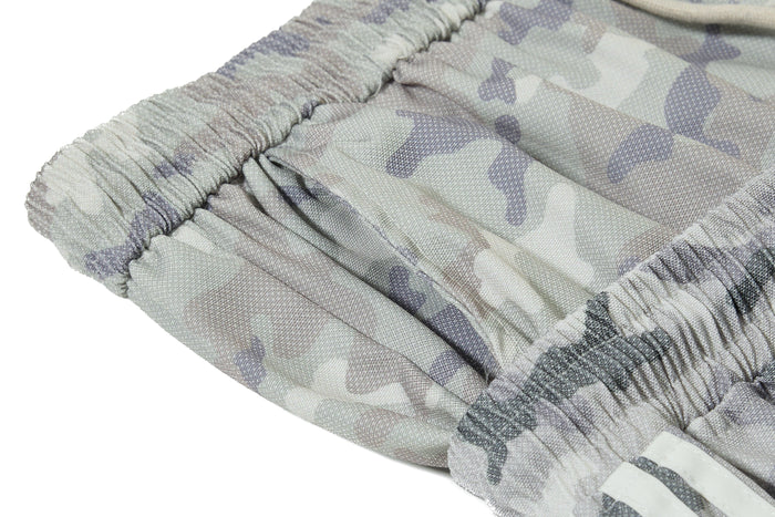 Close-up of cuffed hem and side stripe detail on gray camouflage mesh track pants