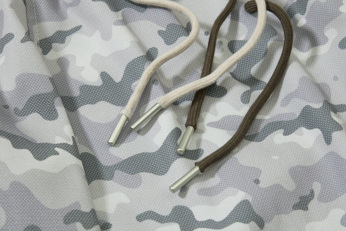 Close-up of two drawstrings with metal tips on gray camouflage mesh track pants