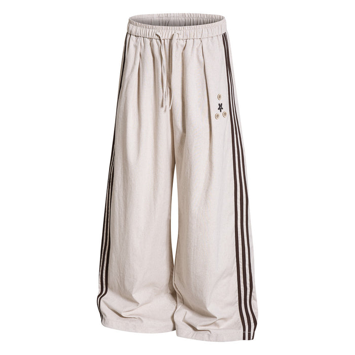 Cream wide-leg track pants front view with triple dark side stripes, elastic drawstring waist and button accents