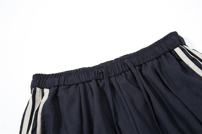 Close-up of navy track pants elastic waistband and cream triple side stripes along the outer leg