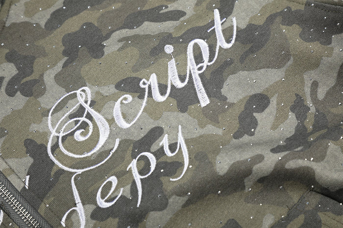 Close-up of white cursive script lettering on glitter-speckled gray-green camouflage fabric