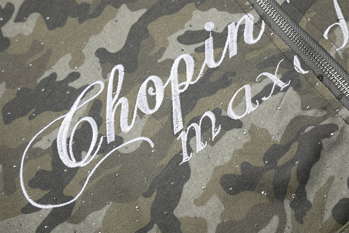 Close-up of white cursive lettering across glitter-speckled gray-green camouflage hoodie fabric